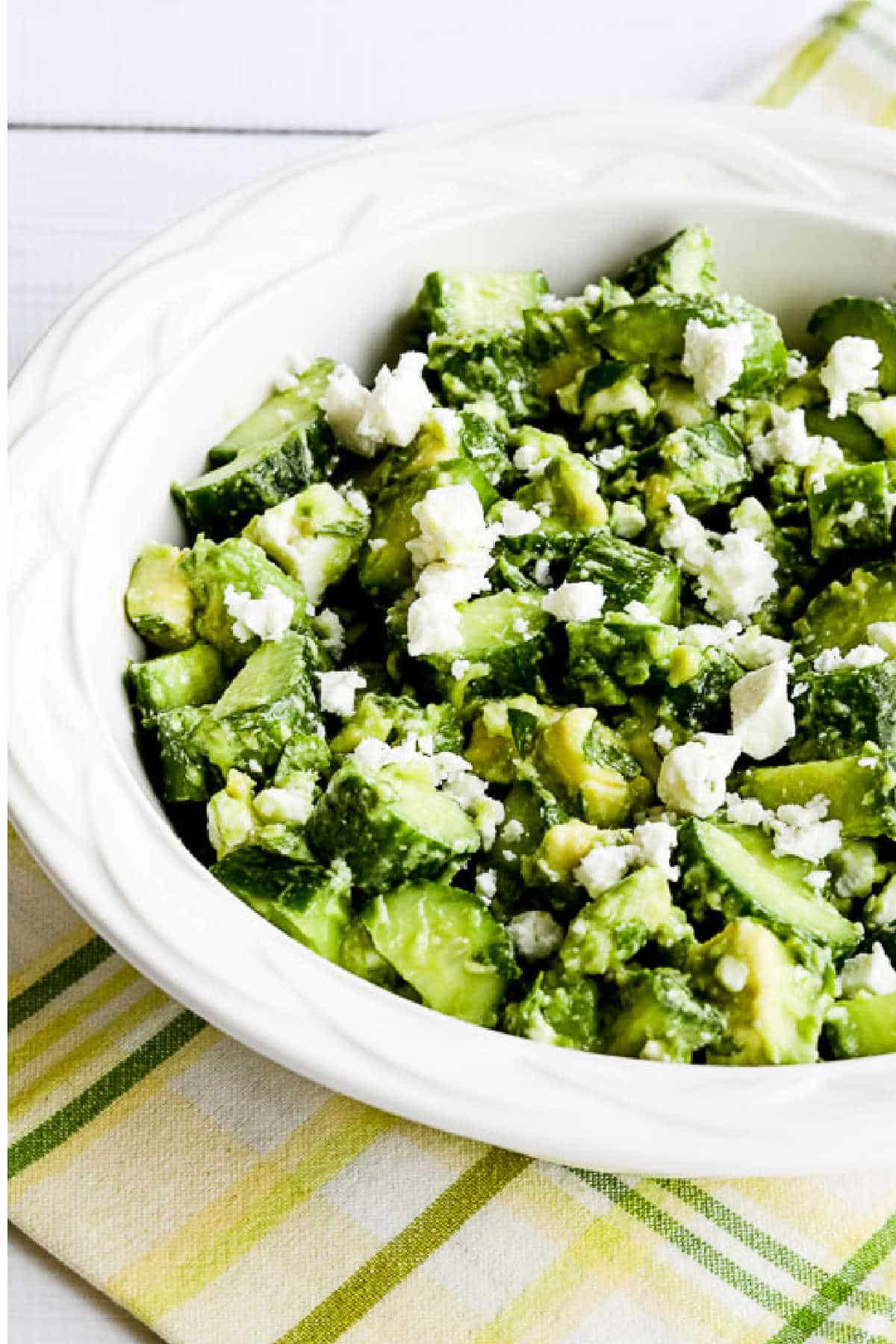 Cucumber Salad with Avocado and Feta shown in serving bowl on yellow-green napkin