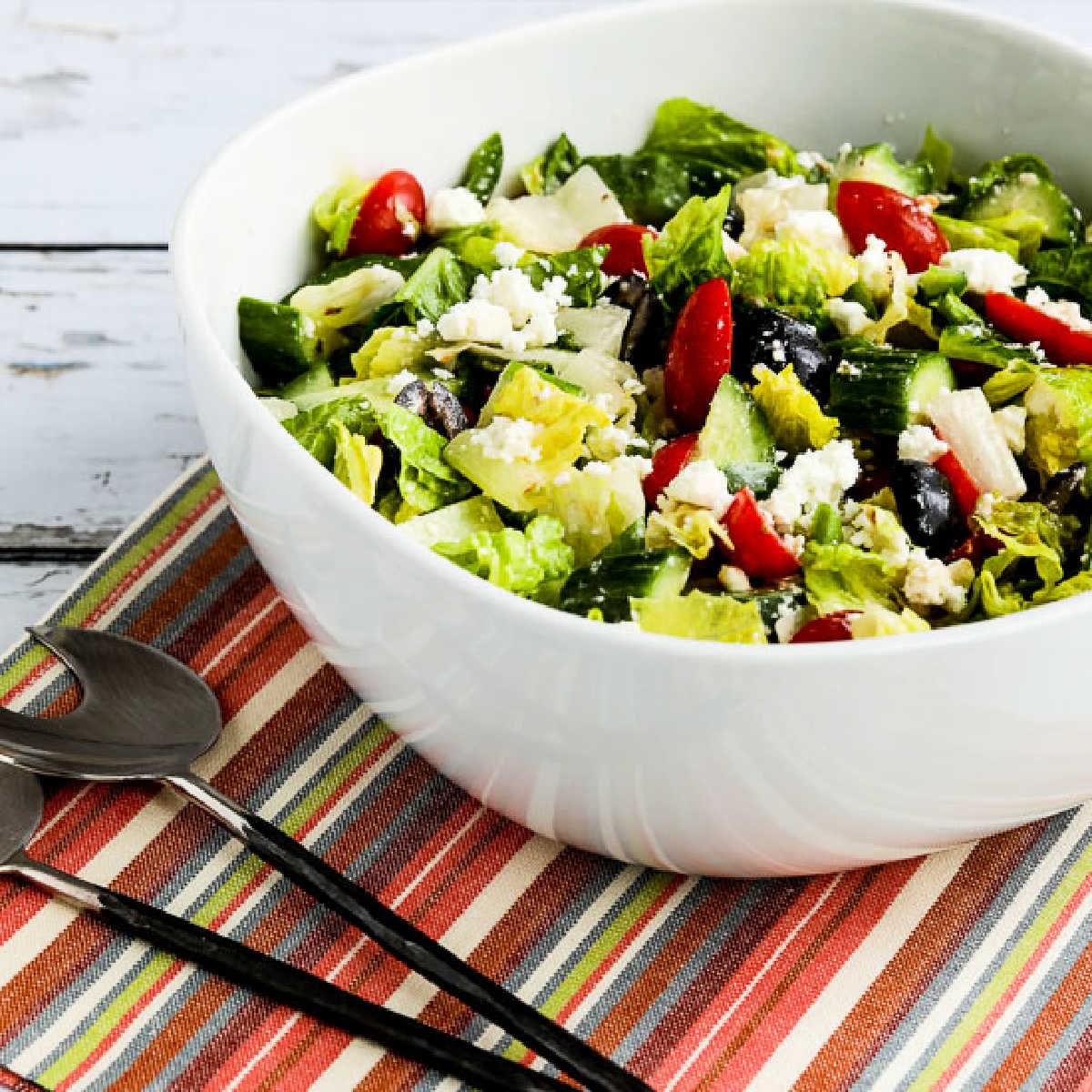 A lettuce Greek salad is shown in a serving bowl with a salad fork.
