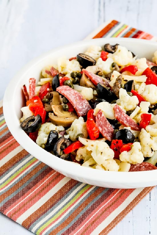 Marinated Cauliflower Antipasto Salad shown in serving bowl on striped napkin