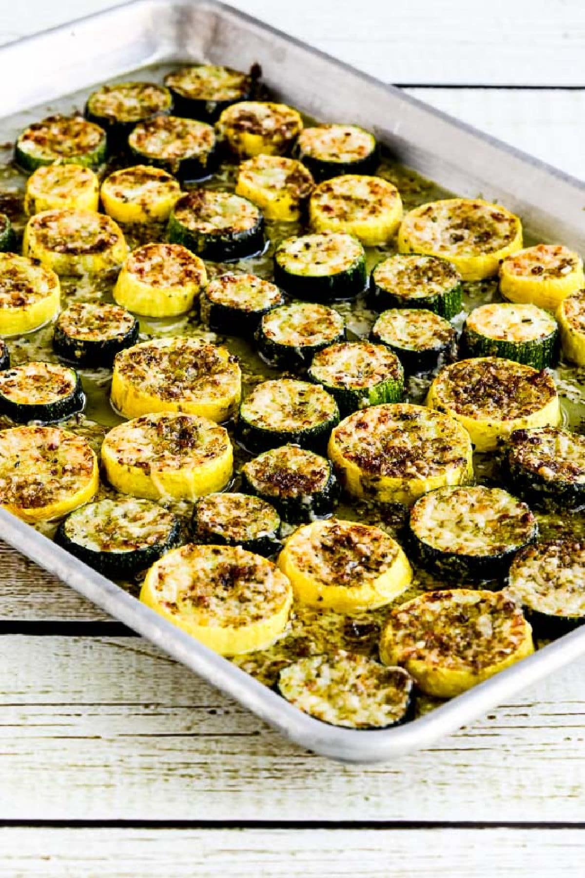 Summer Squash with Pesto and Parmesan on baking sheet on wooden background