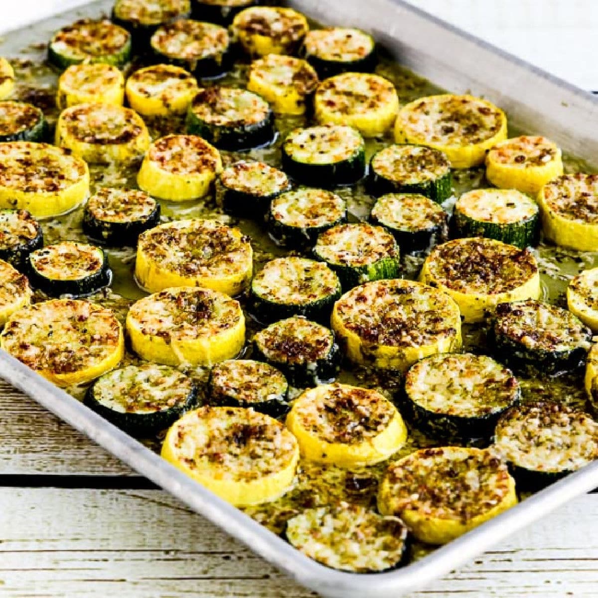 Square picture of summer squash with pesto and parmesan on baking tray