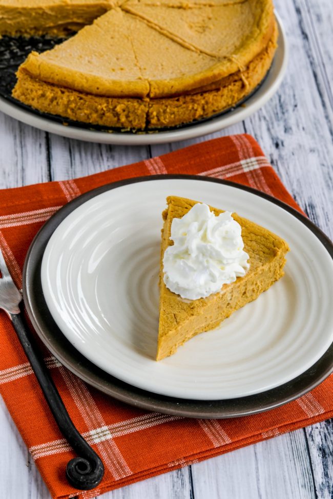 Sugar-free pumpkin cheesecake displayed on a serving plate with pie in the background