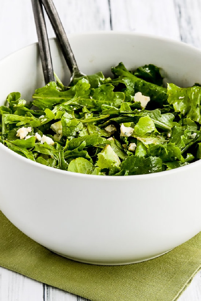 Kale and Arugula Salad in bowl with metal serving spoons.