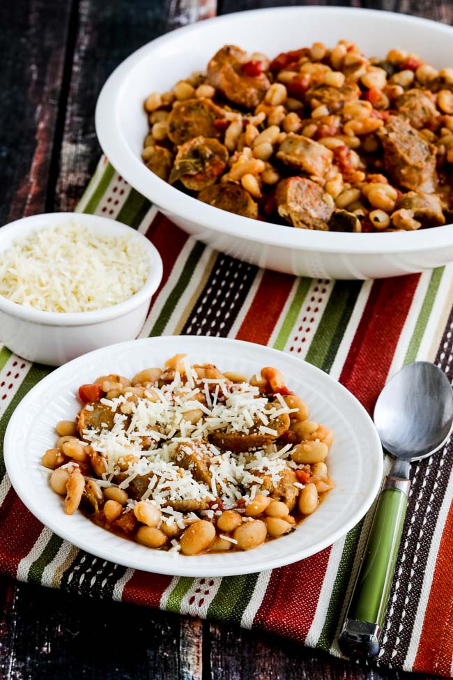 Italian Sausage and White Beans with Sage shown in large serving dish and one serving bowl with spoon and parmesan