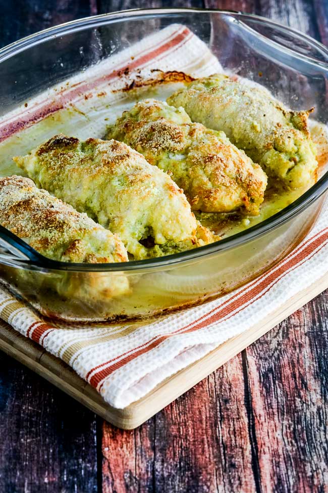Baked Chicken Stuffed with Pesto and Cheese shown in baking dish on towel on cutting board