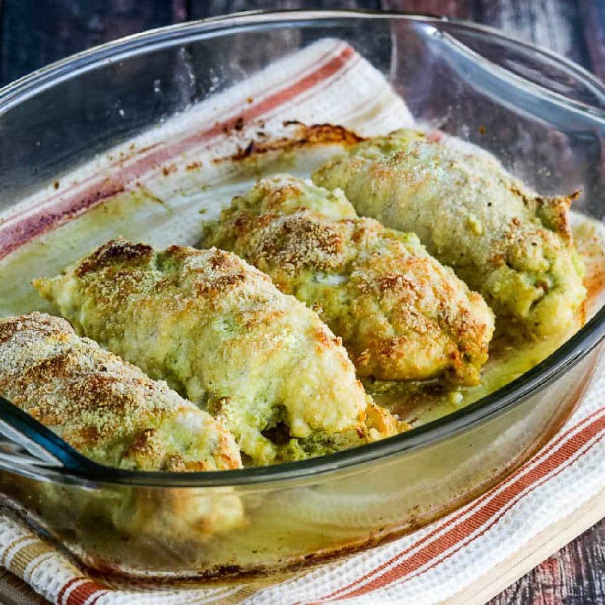 Baked Chicken Stuffed with Pesto and Cheese shown in baking dish on towel.