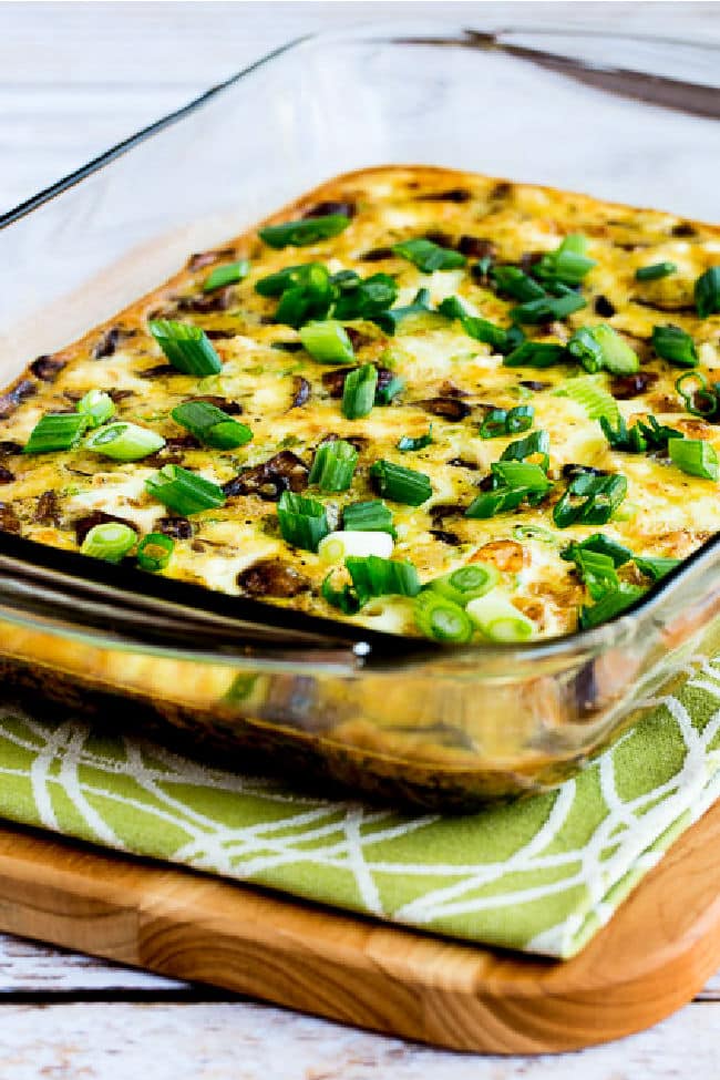 Sausage, Mushrooms, and Feta Baked with Eggs shown in baking dish on napkin and cutting board.