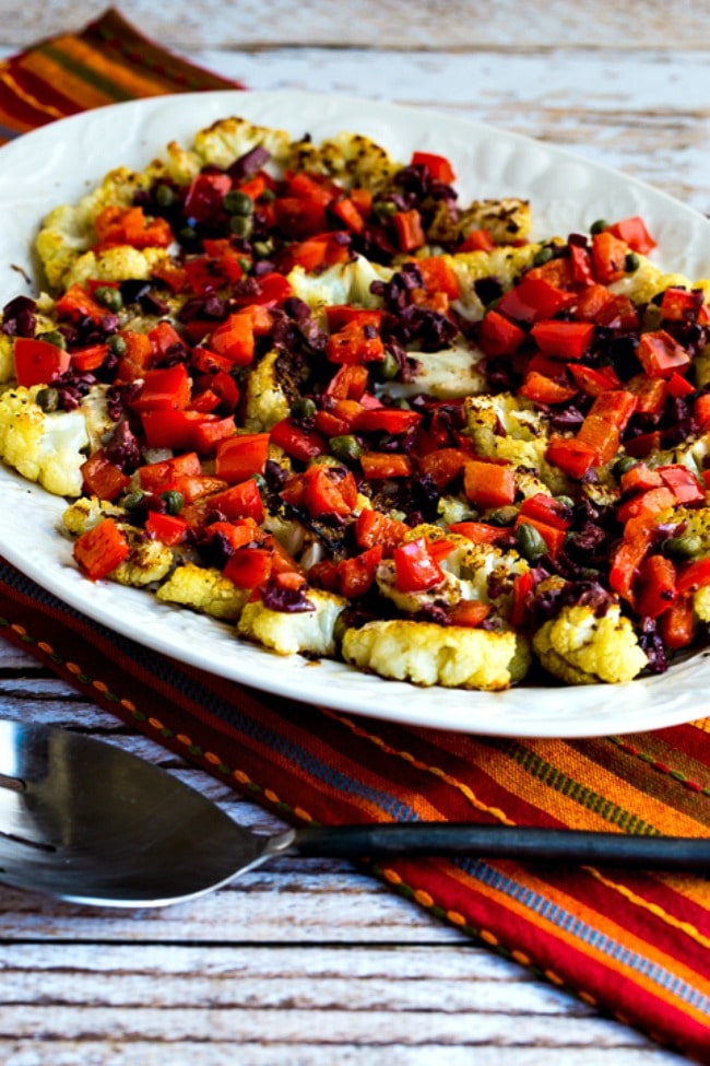 Roasted cauliflower slices with red pepper, capers and olives in a serving dish