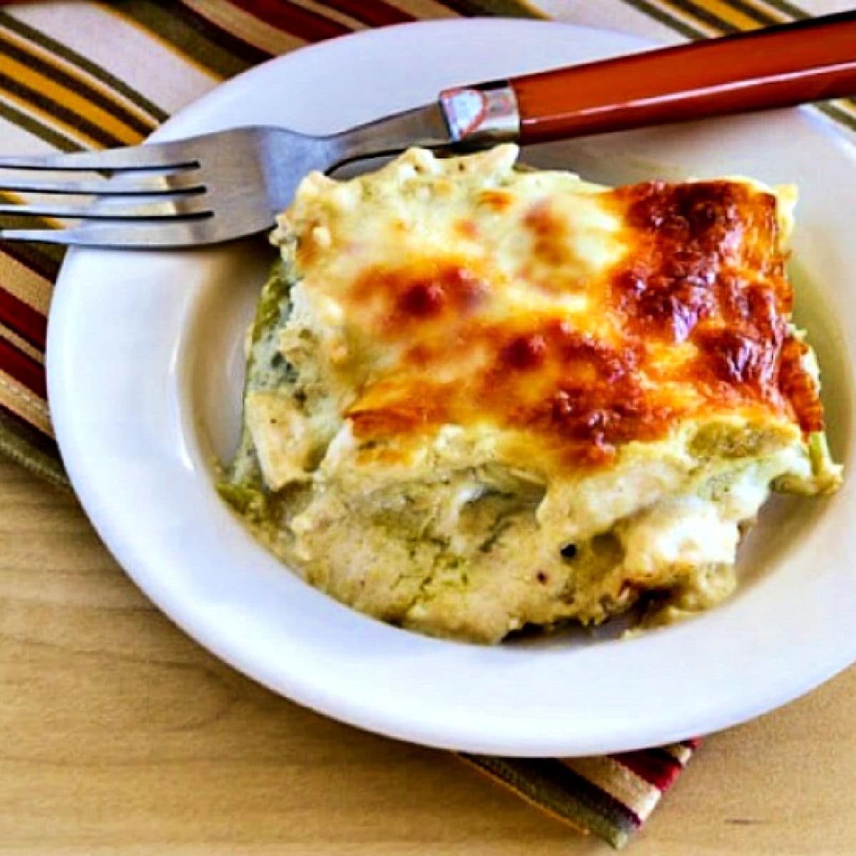 Square image of Green Chile and Chicken Mock Enchilada Casserole with one serving on plate with fork.
