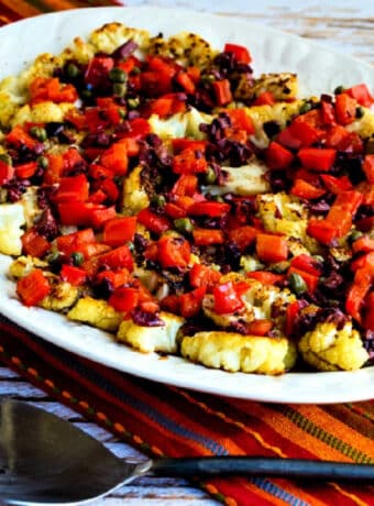Roasted Cauliflower Steaks with Red Pepper, Capers, and Olives shown on serving platter with serving spoon
