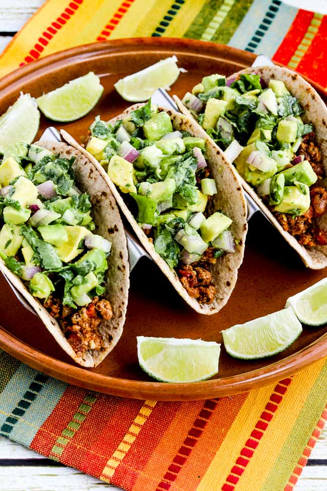 Tacos with avocado salsa on serving plate with limes and colorful napkin