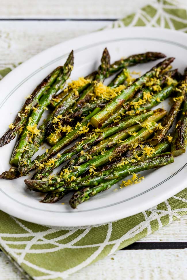 Fried Asparagus Tips with Lemon Juice and Lemon Zest shown on serving plate on green-white napkin.