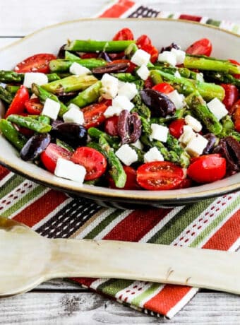 Square image of Asparagus Salad with Tomatoes, Olives, and Feta in serving bowl on colorful napkin.