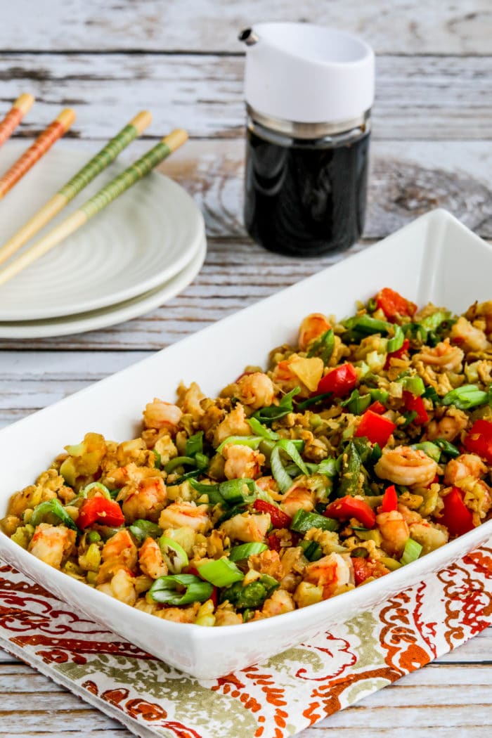 Cauliflower Fried Rice with Shrimp shown in serving bowl with soy sauce and chopsticks in background