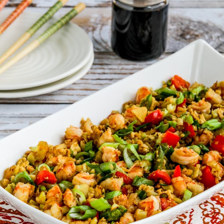 Cauliflower Fried Rice with Shrimp shown in serving bowl with soy sauce and chopsticks in background