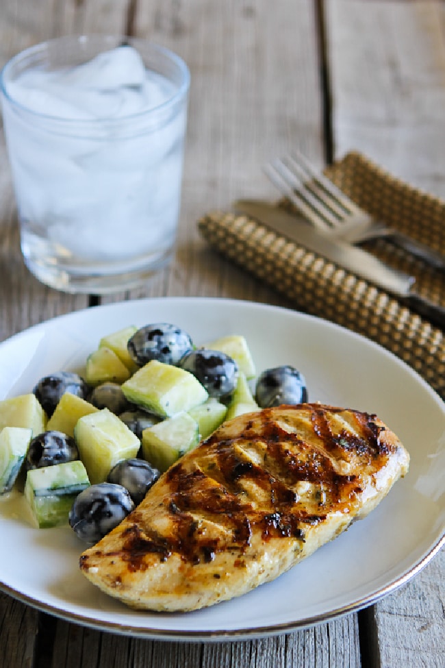 Grilled Chicken with Lemon, Capers, and Oregano on serving plate, with water glass, silverware, and napkin