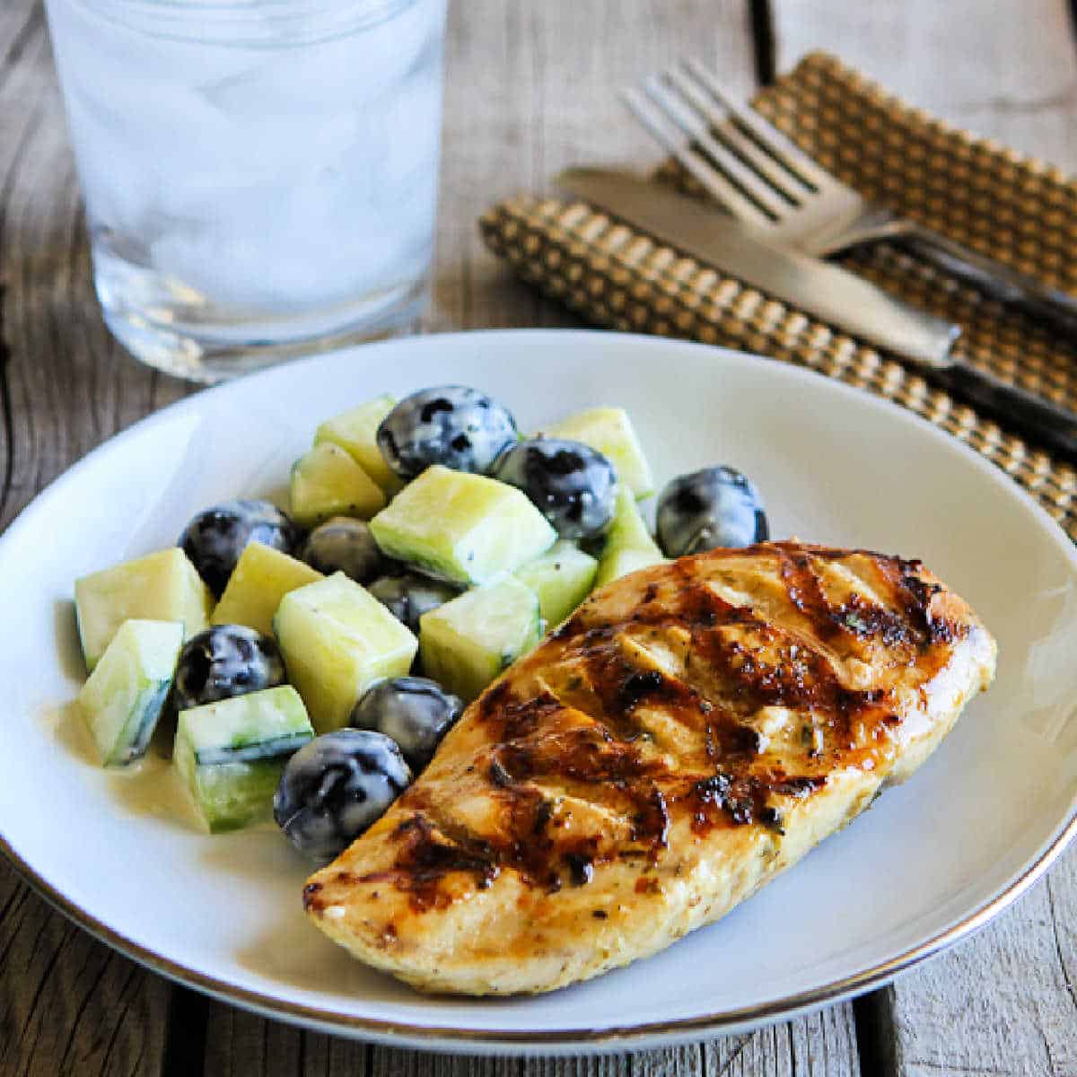 Grilled chicken with lemon and capers A square picture of chicken on a plate with cucumber olive salad