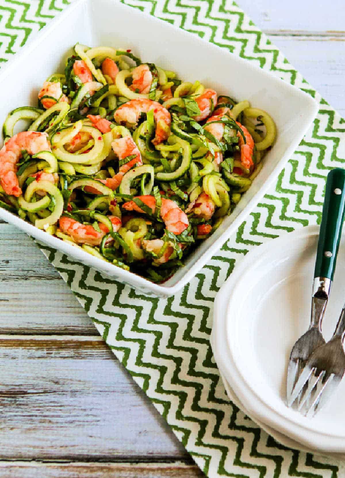 Cucumber Noodle Salad with Shrimp shown in serving bowl with napkin, plates, and forks
