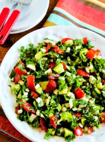 Square image of Middle Eastern Tomato Salad shown in serving bowl with plates and forks on the side.