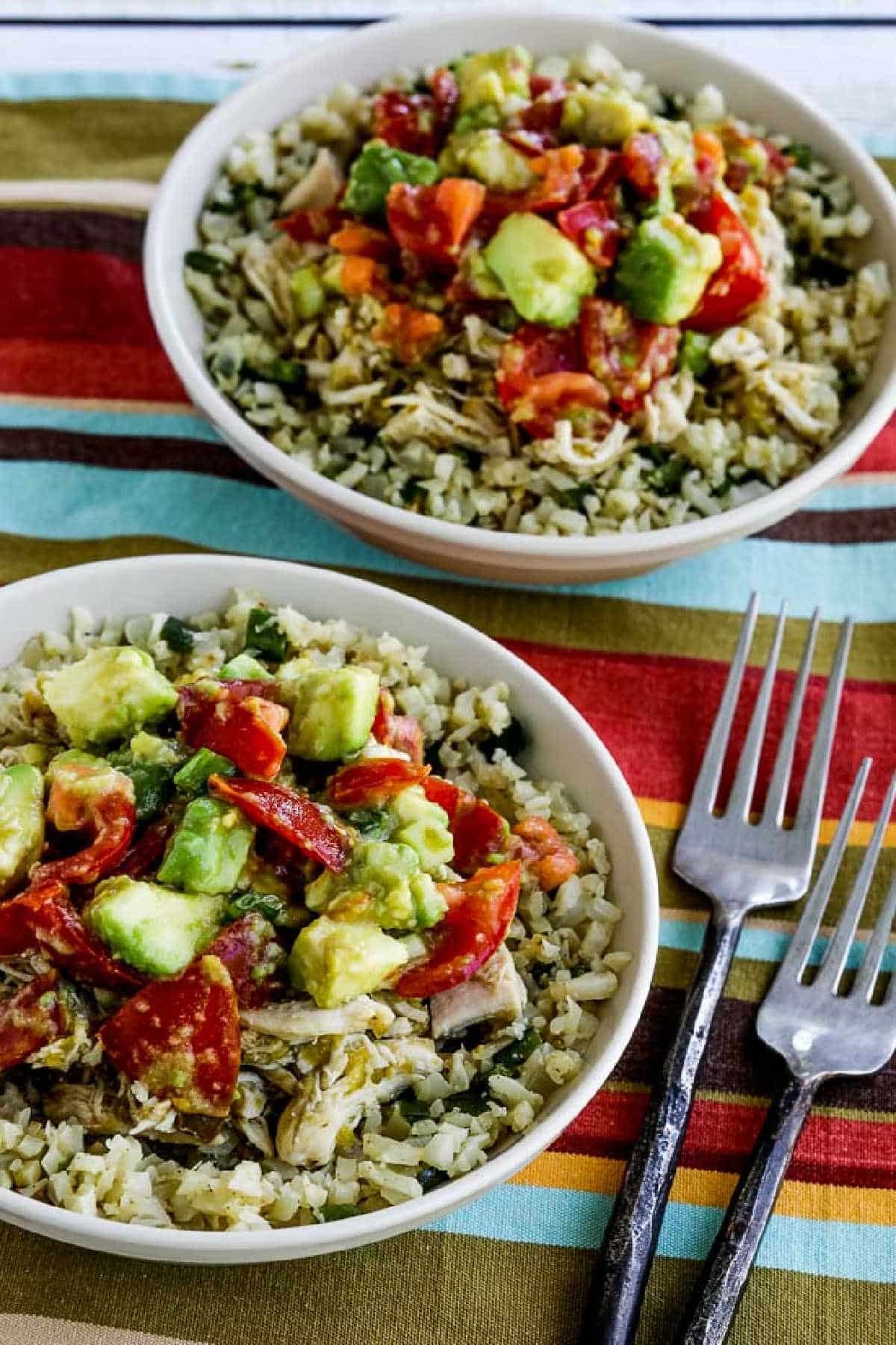 Instant Pot Green Chile Chicken Burrito Bowl shown in two bowls with forks and striped napkin.