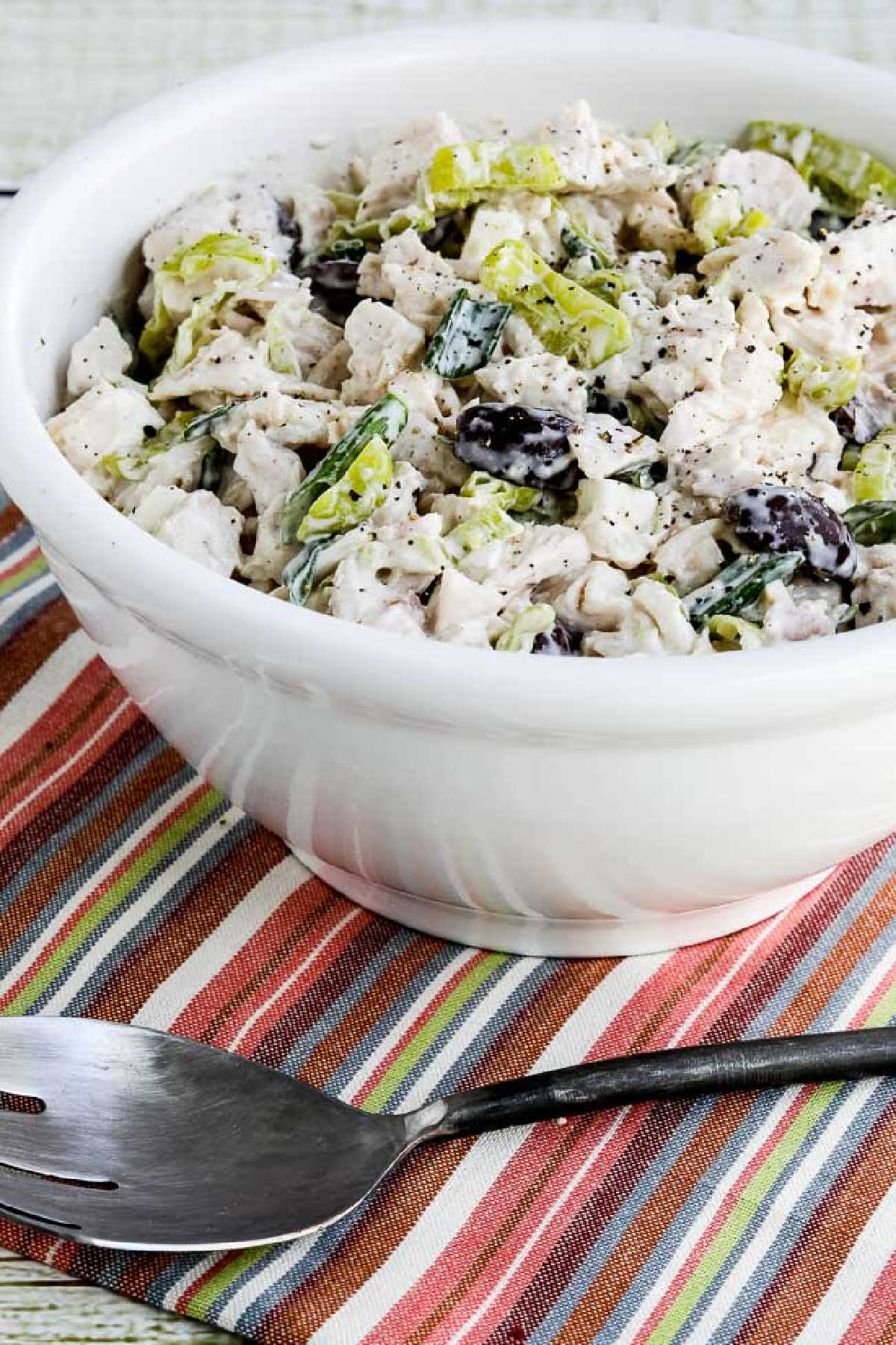 Greek Chicken Salad with Peperoncini shown in serving bowl in striped napkin