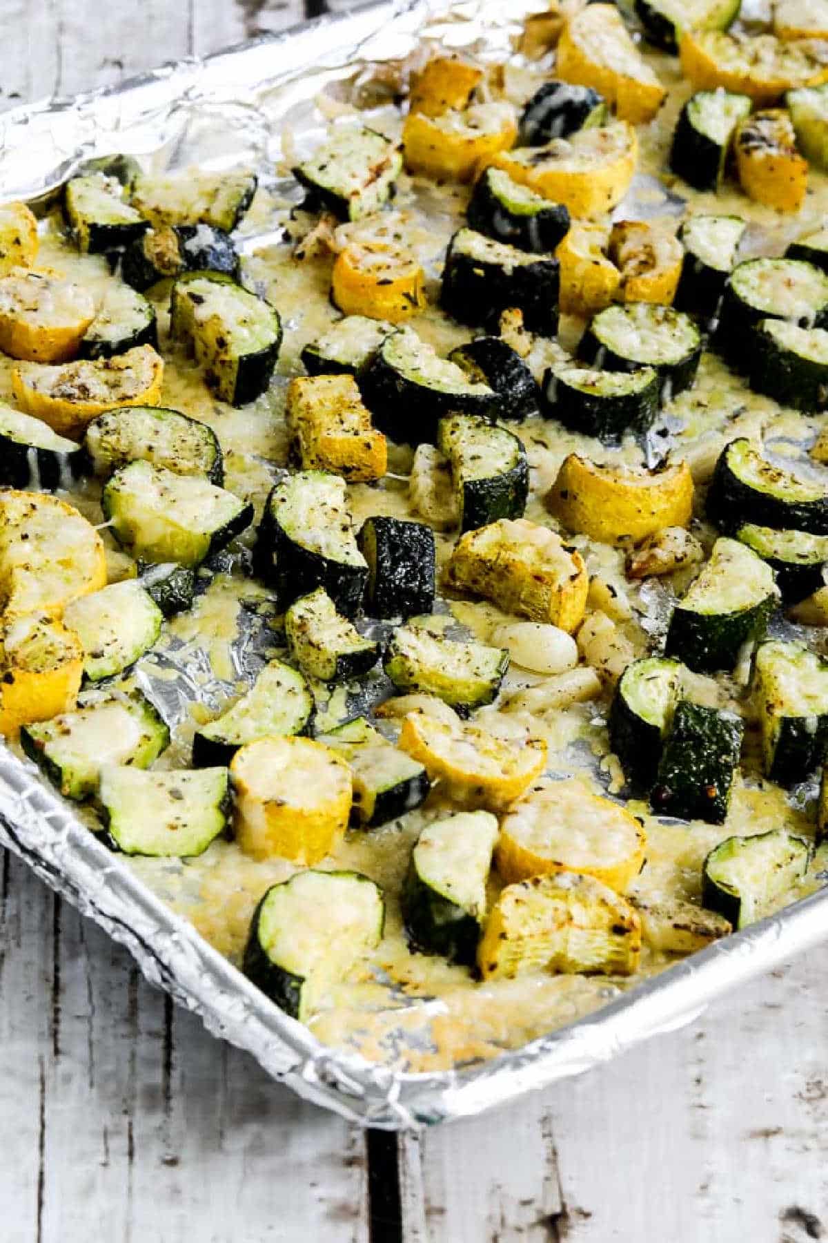 Roasted summer squash with garlic and parmesan cheese on a baking sheet at a wooden table