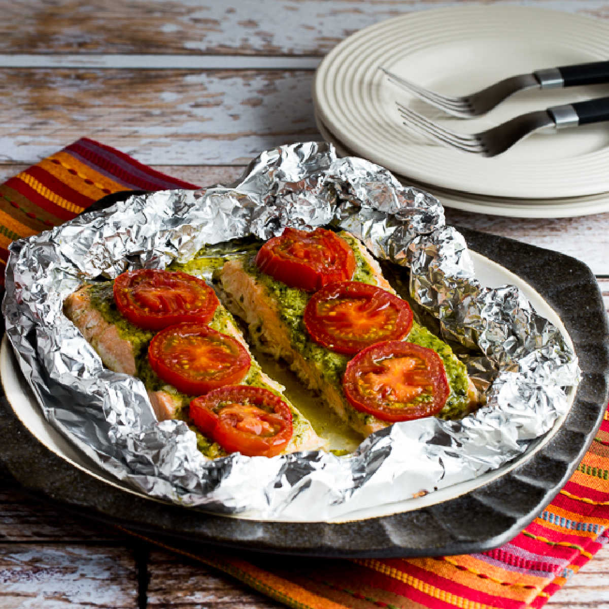 Baked Salmon with Pesto and Tomatoes shown with foil on serving plate.