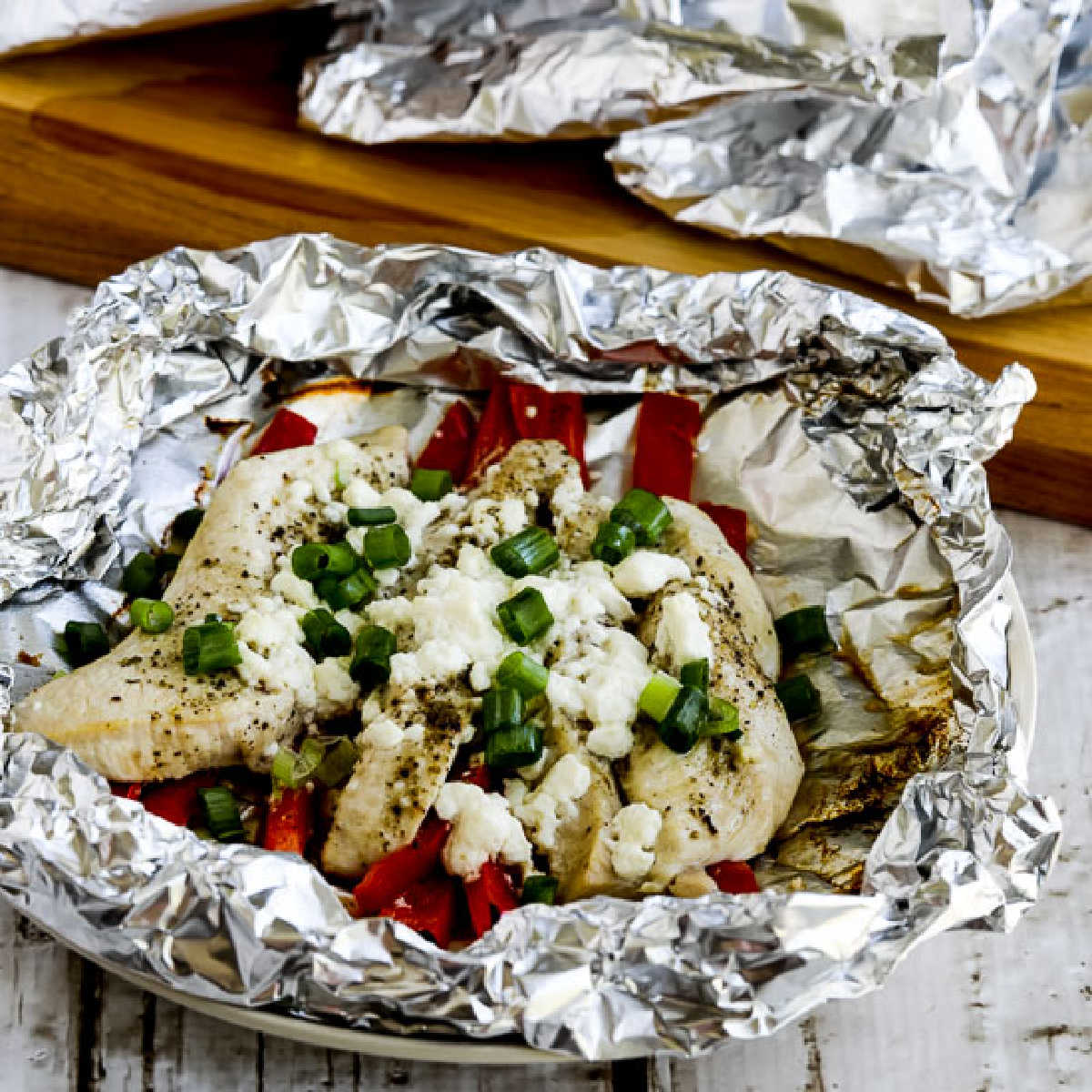 Greek Chicken Foil Packets with one packet open and wrapped ones in back.