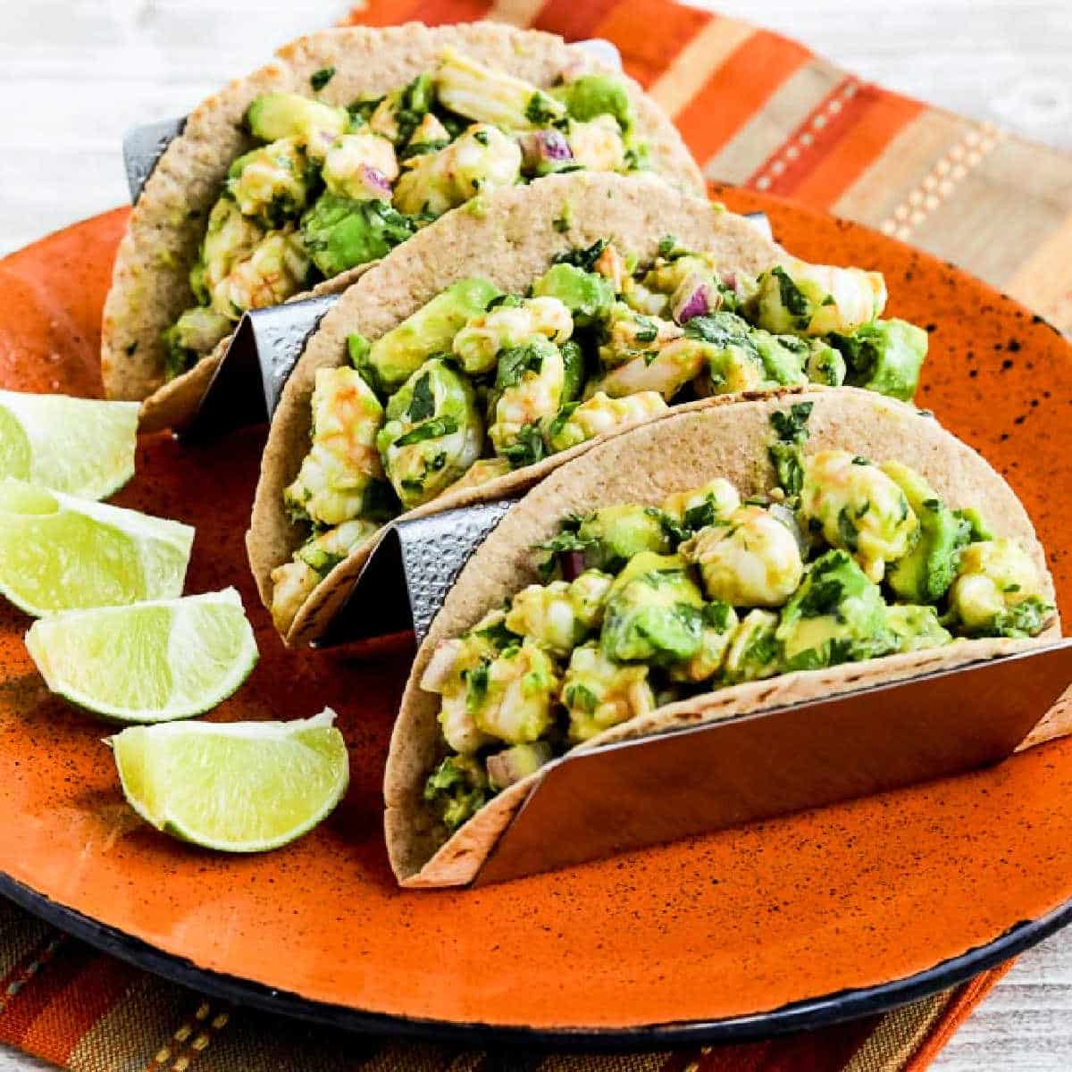 Square image of three Shrimp Avocado Tacos shown on serving plate with lime.