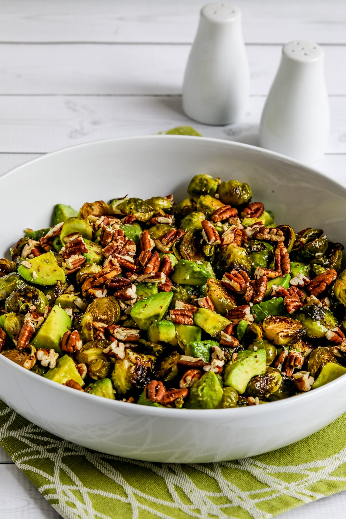 Roasted Brussels Sprouts with Avocados and Pecans shown in serving bowl on green-white napkin