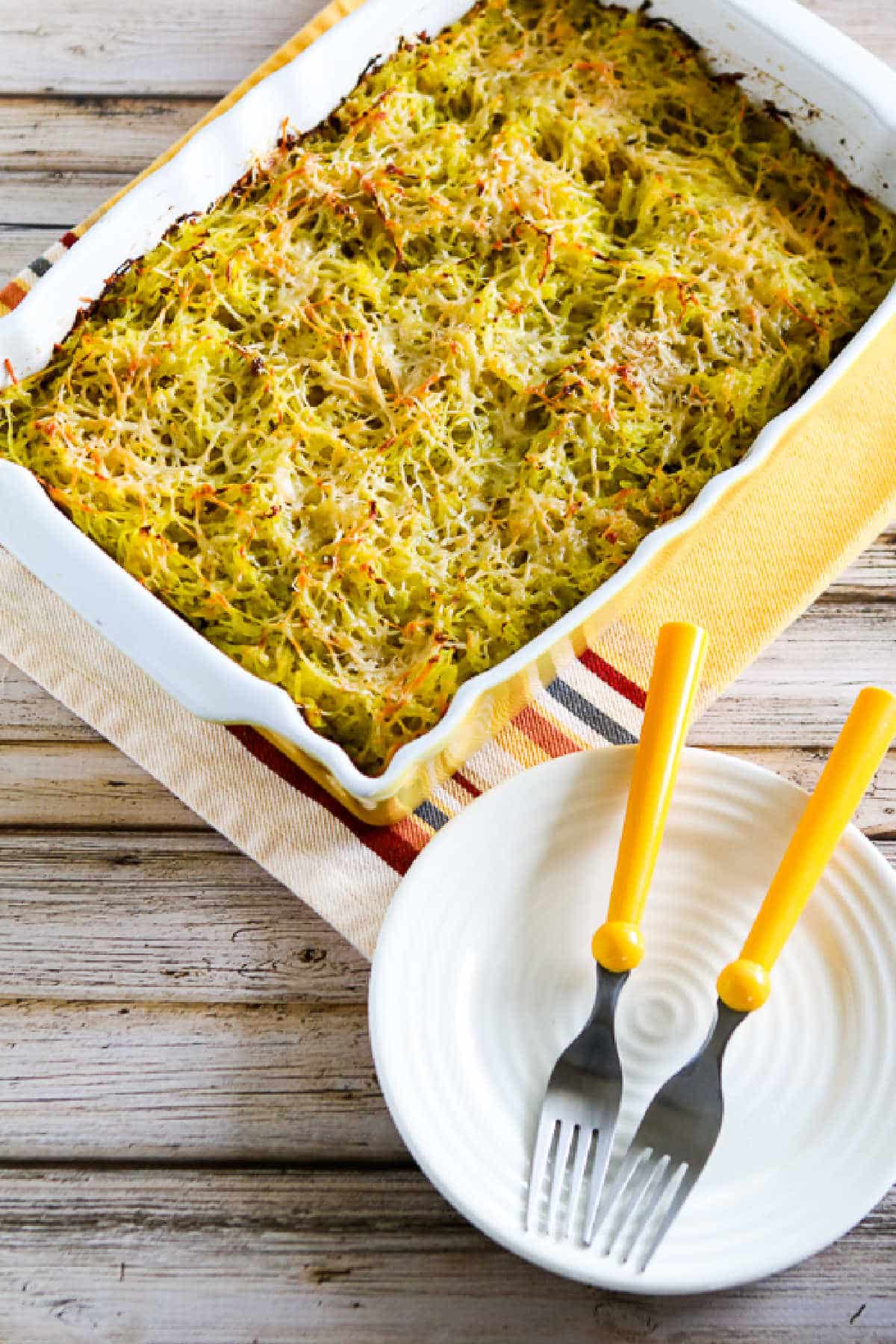 Baked squash spaghetti with pesto in a serving dish with plates and forks