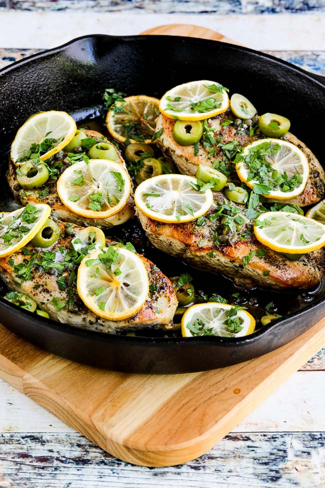 Skillet Chicken with Lemon, Green Olives, and Capers shown in skillet on cutting board.