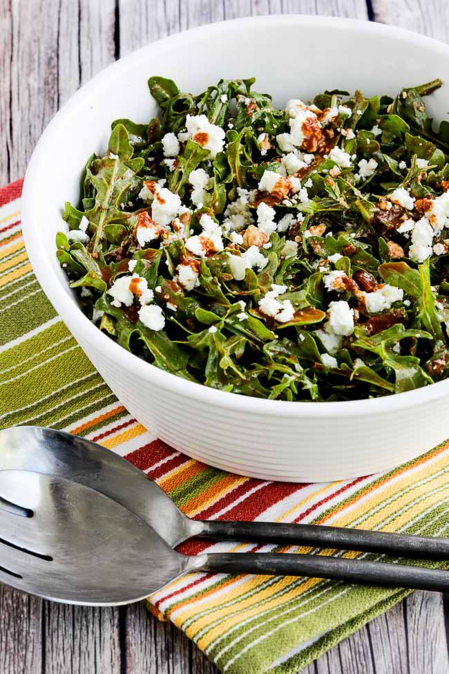 Arugula salad with feta shown in a serving bowl with serving forks