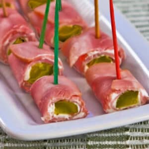 Large square image of ham and pickle roll ups shown on serving plate.