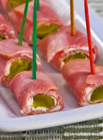 Large square image of ham and pickle roll ups shown on serving plate.