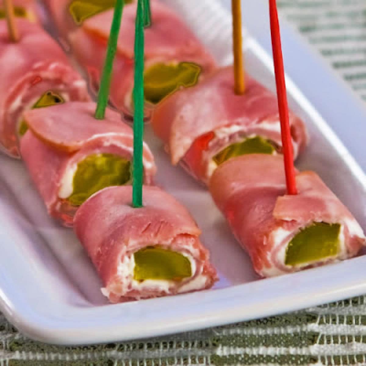 Large square image of ham and pickle roll ups shown on serving plate.