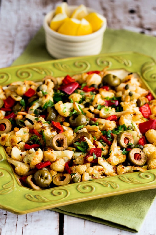 Roasted cauliflower topped with red peppers, green olives and pine nuts on a serving platter
