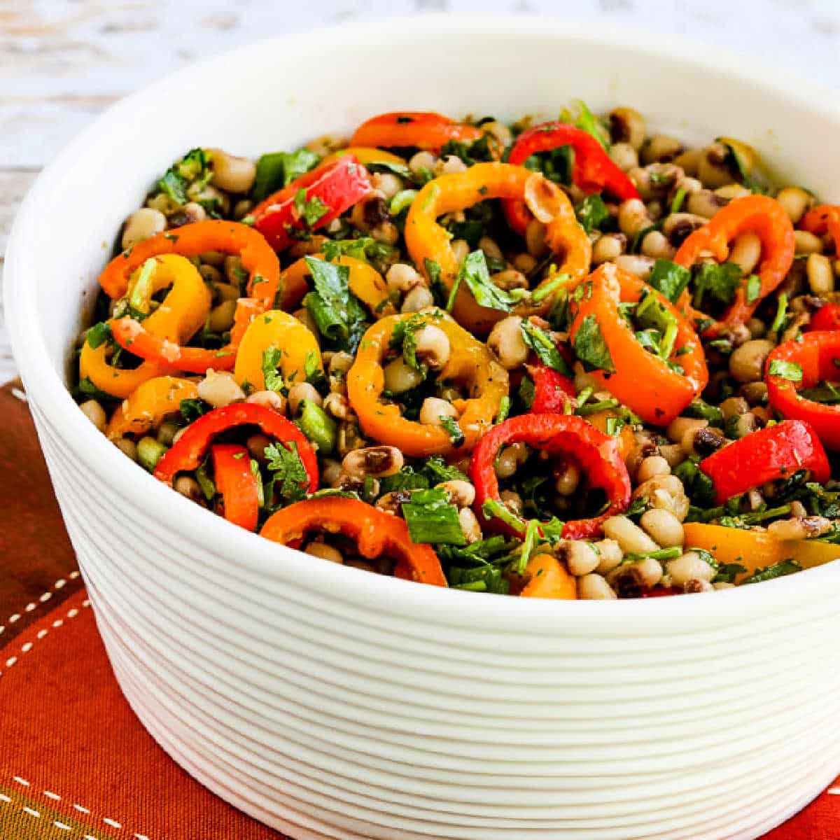 Square image of Black-Eyed Pea Salad with Peppers, Cilantro, and Cumin-Lime Vinaigrette shown in white bowl on napkin.