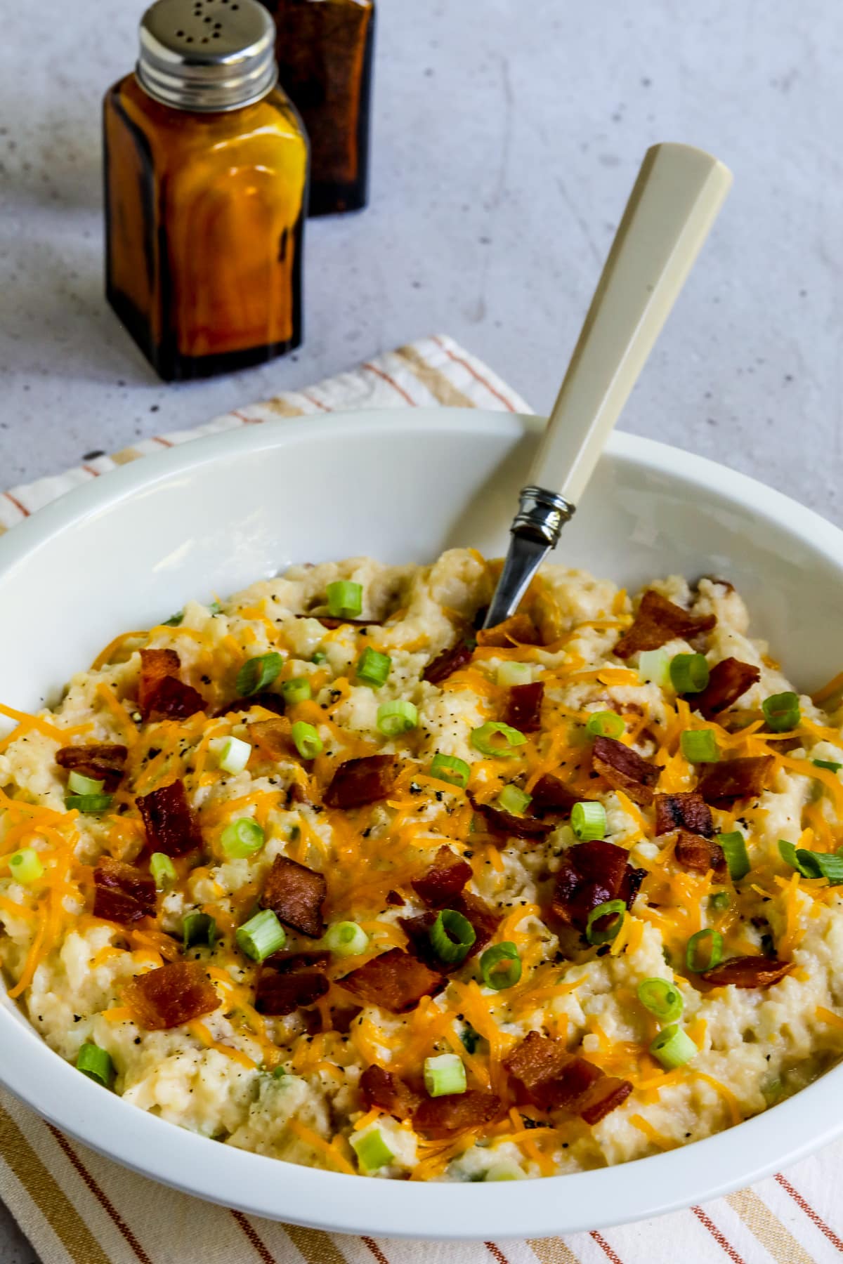 Loaded Cauliflower Mash (Instant Pot or Stovetop) shown in serving bowl with salt-pepper in back.