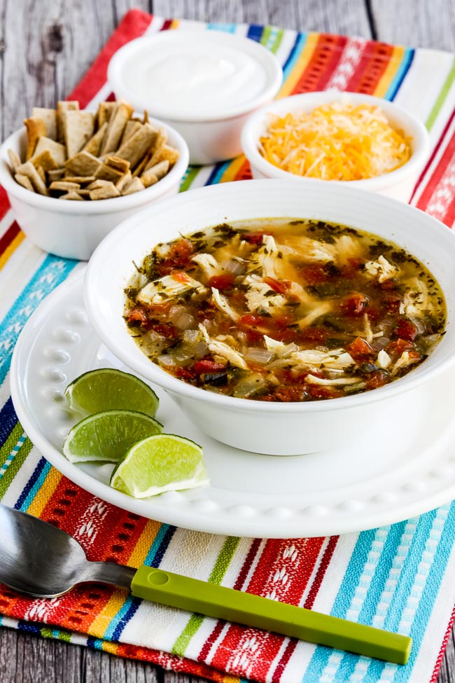 Instant Pot Chicken Tortilla Soup shown in bowl with limes, cheese, and tortila strips