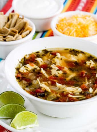 square image of Instant Pot Chicken Tortilla Soup in serving bowl with tortilla strips, cheese, and sour cream in background