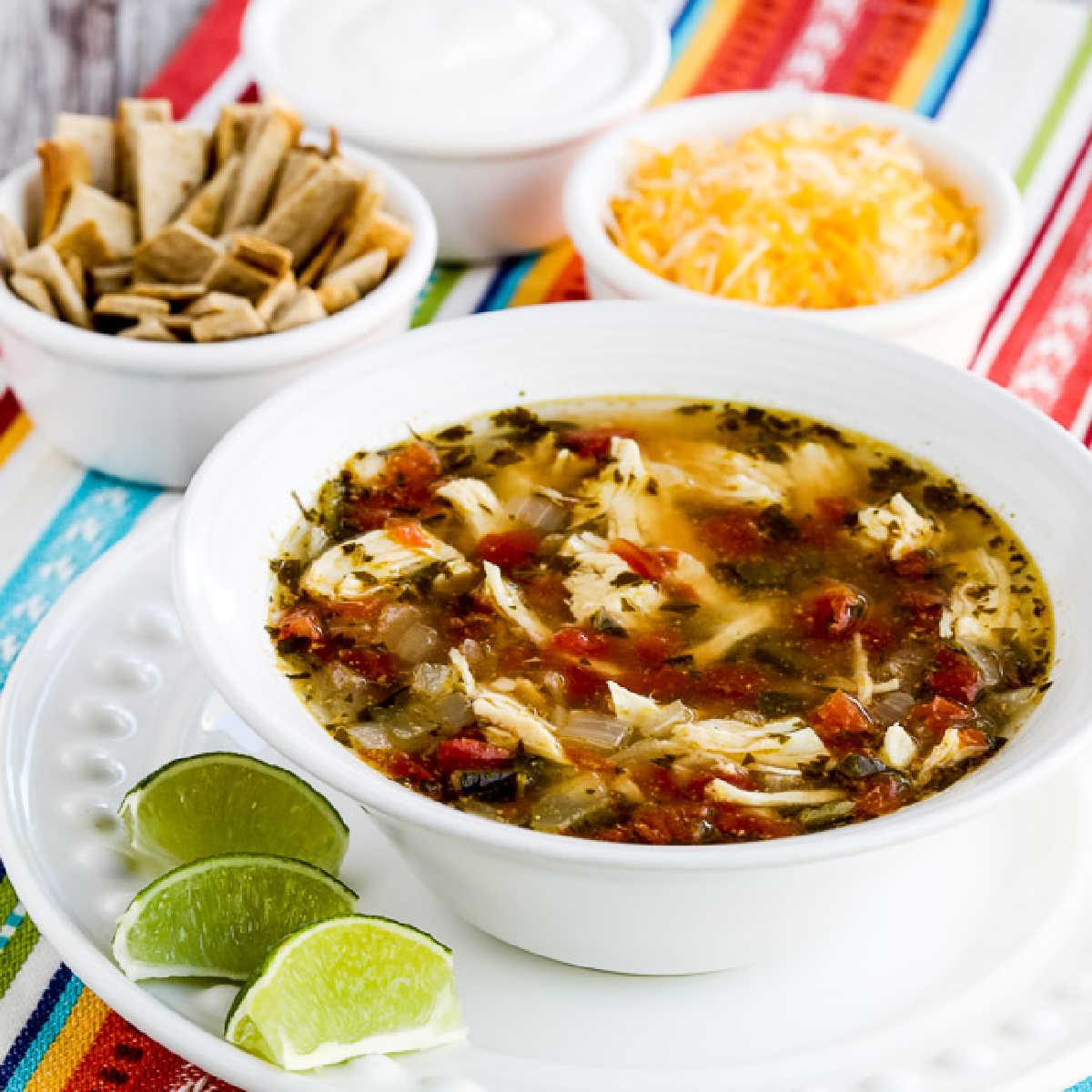 square image of Instant Pot Chicken Tortilla Soup in serving bowl with tortilla strips, cheese, and sour cream in background