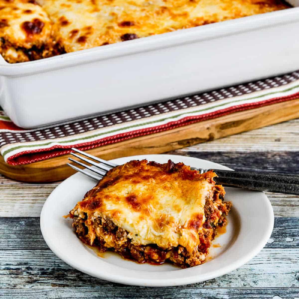 Square image of no noodle lasagne with sausage and basil.  One dish is served on a plate with a casserole dish in the background.