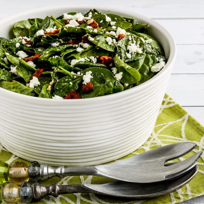 square image of spinach salad with bacon and feta in a serving bowl with forks