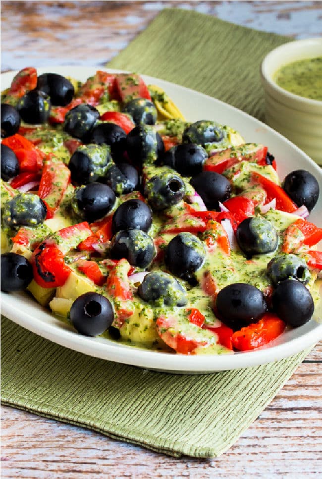 Antipasto Artichoke Salad with Basil Vinaigrette shown on serving platter with basil vinaigrette on the side.