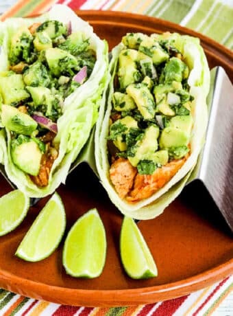 Square image of Spicy Shredded Chicken Lettuce Wrap Tacos on serving plate in taco holder, with limes.