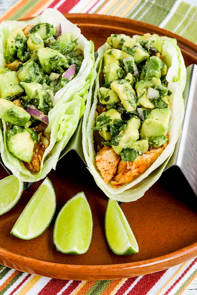 Spicy Shredded Chicken Lettuce Wrap Tacos close-up view of tacos on serving plate, with limes.