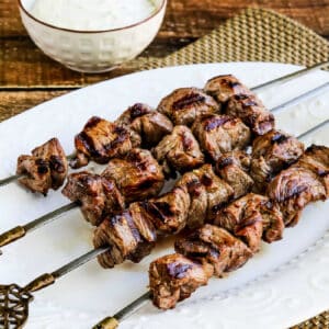 Greek Lamb Souvlaki shown on serving plate with Tzatziki in background.