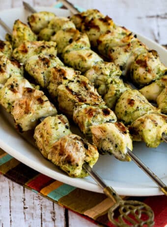 Square image of Lemon Pesto Chicken Kabobs shown on serving plate on striped napkin.