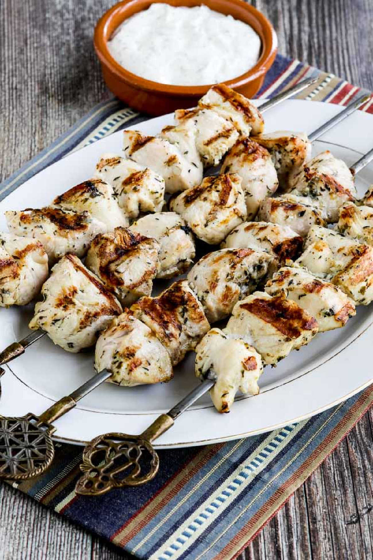 Chicken Souvlaki on serving platter with Tzatziki sauce, on blue striped napkin